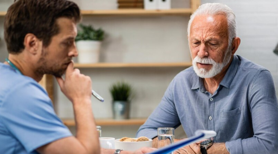 A senior man speaking with a young healthcare professional.