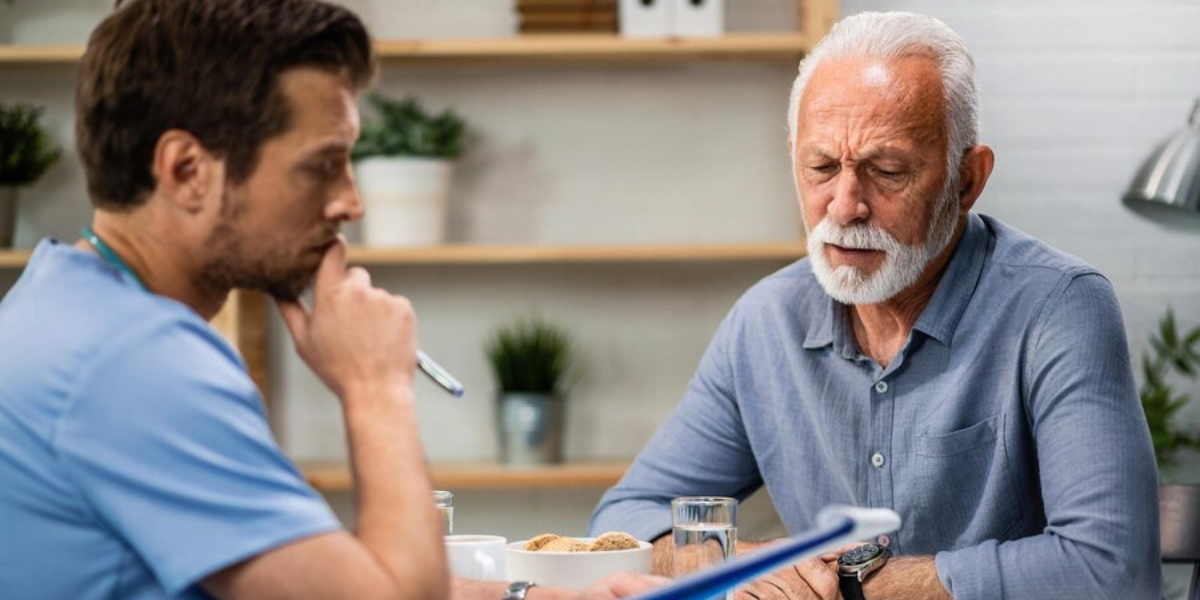 A senior man speaking with a young healthcare professional.