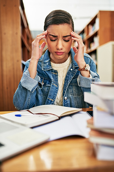 teen girl holding her head and looking sad with stacks of books and paper on table