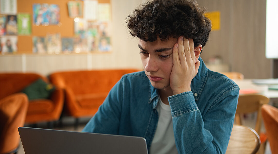 stressed teen holding head and looking at computer