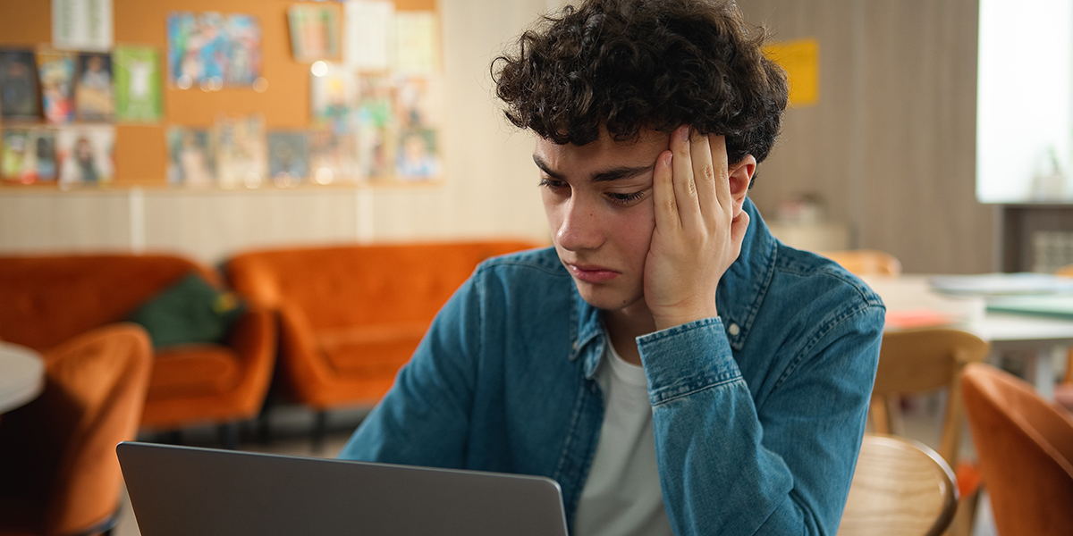 stressed teen holding head and looking at computer