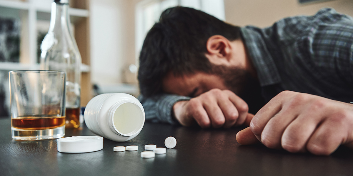 man laying with his head on arm with open bottle of pills and alcohol