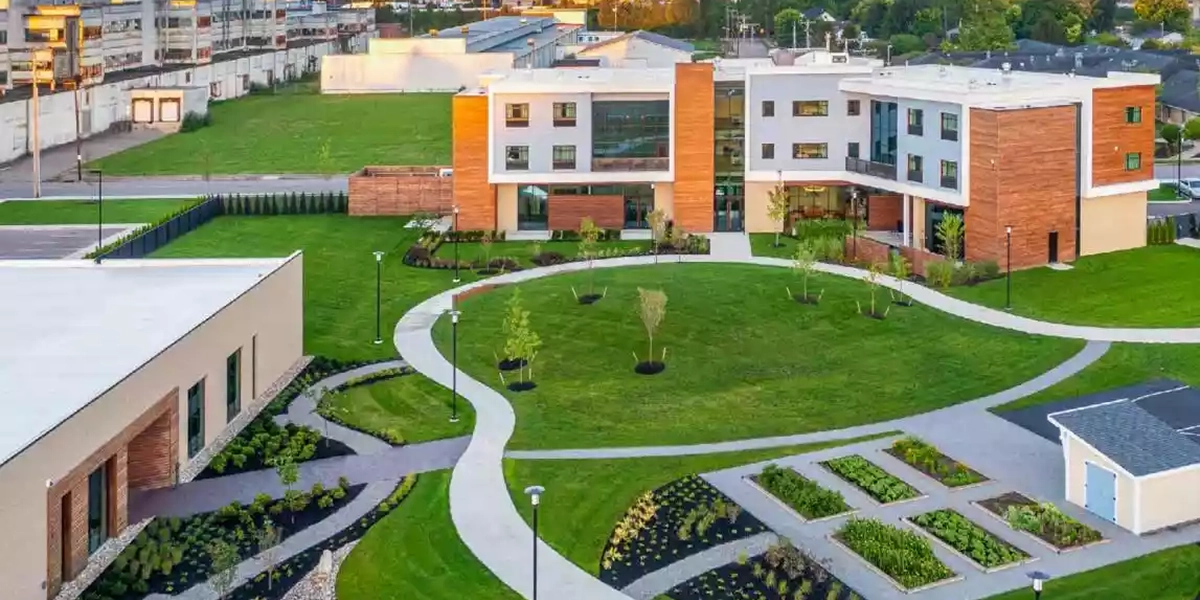 Modern campus quad with curved concrete paths, green lawns, and contemporary buildings with wood and white facades.