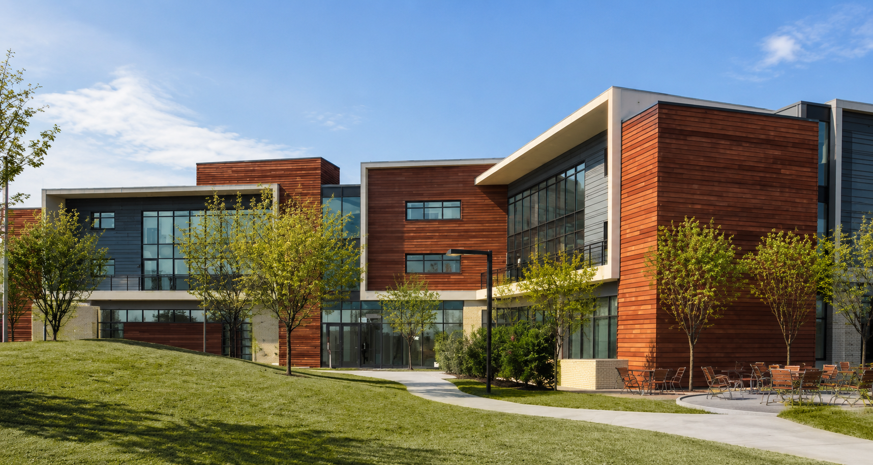 Modern campus-style building with wood paneling, large glass walls, and green landscaping under a blue sky.