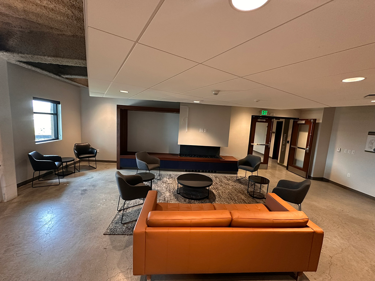 Modern lounge with an orange sofa, gray chairs, and circular coffee tables around a rug and a built-in fireplace/entertainment wall.