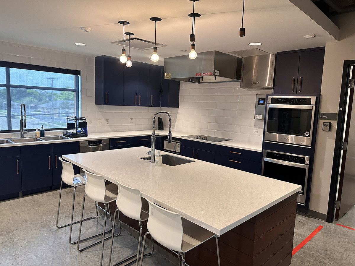 Modern kitchen with a large white island, navy cabinets, and stainless steel appliances; pendant lights hang over the island.