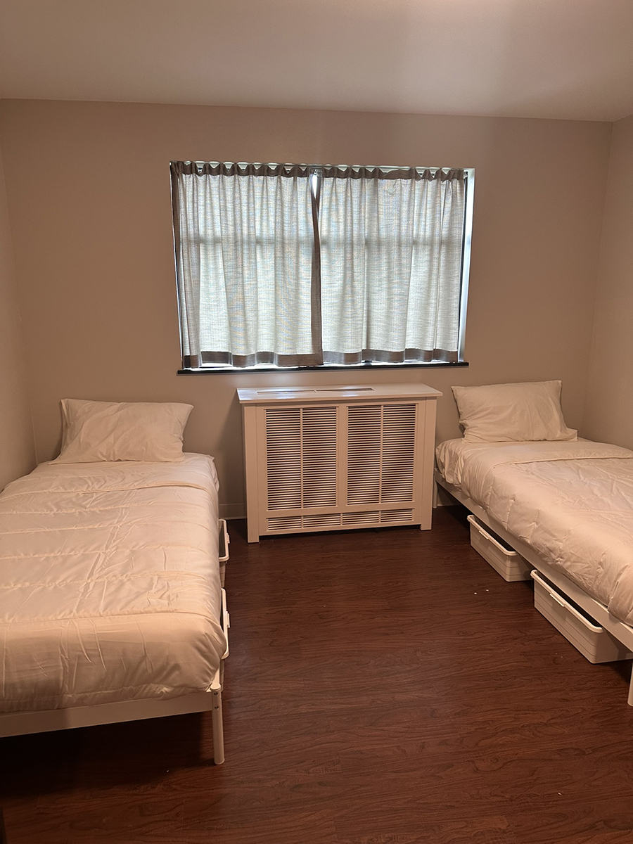 Twin bedroom with two single beds and a radiator cover between them under a curtained window.